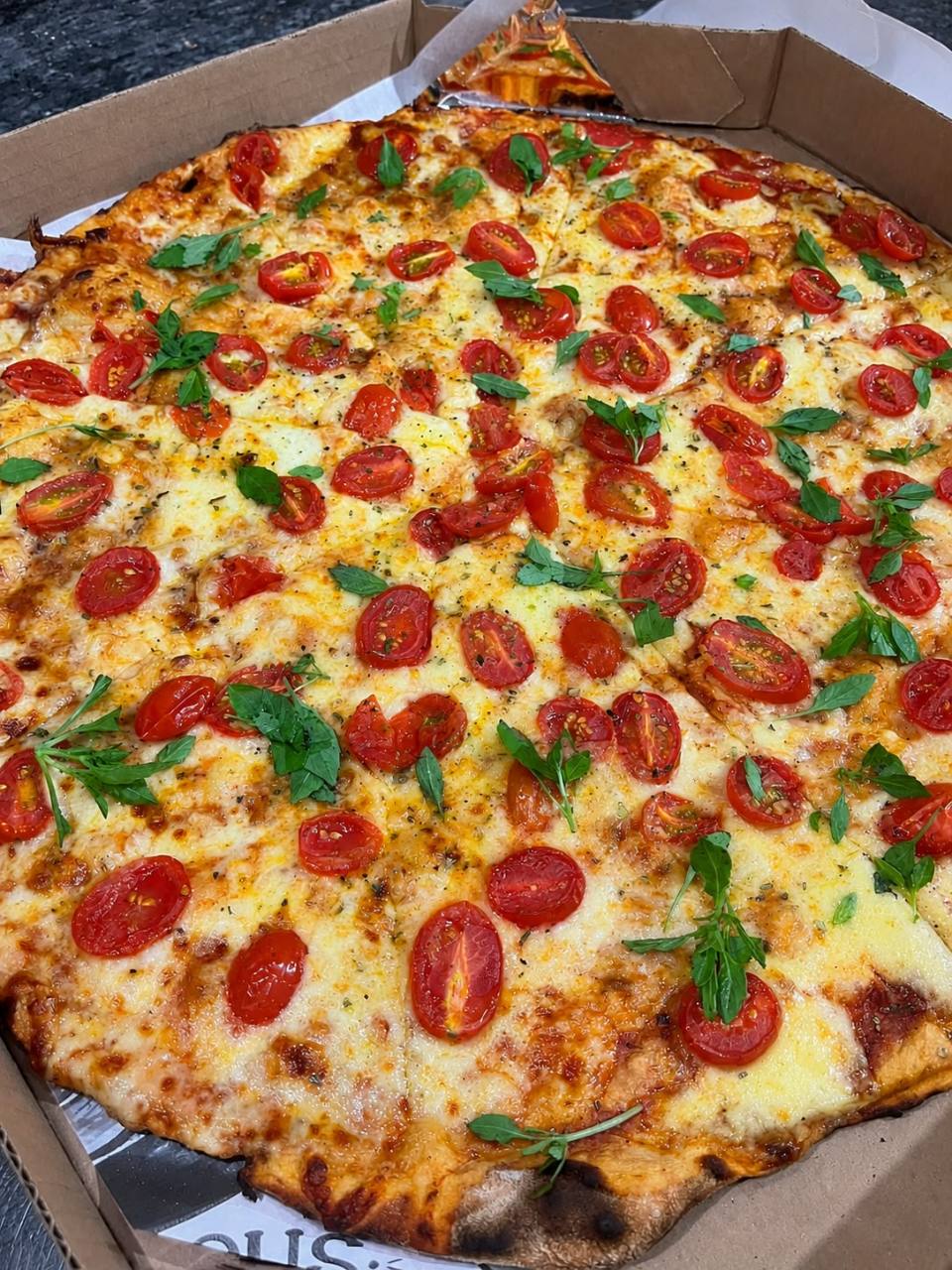 Pizza da Home Pizzas com queijo, tomate e folhas verdes